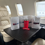 Airplane seat with a tray table featuring a red cup and coffee packages.