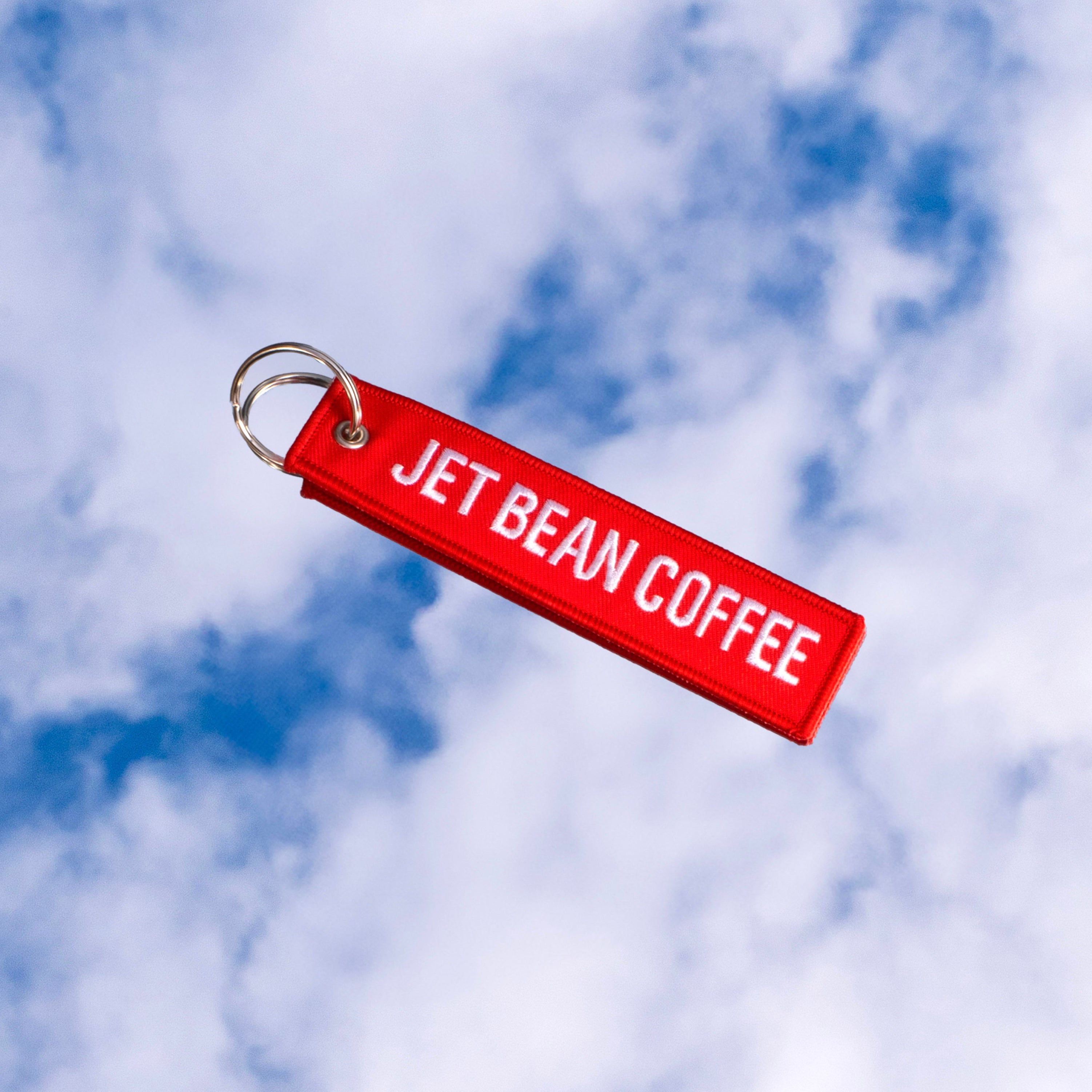 Red keychain with 'JET BEAN COFFEE' text against a cloudy sky background